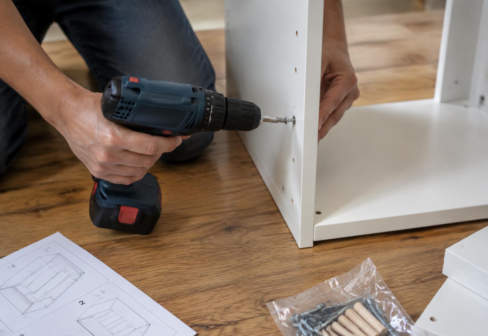 Hands assembling a white cabinet with a cordless drill